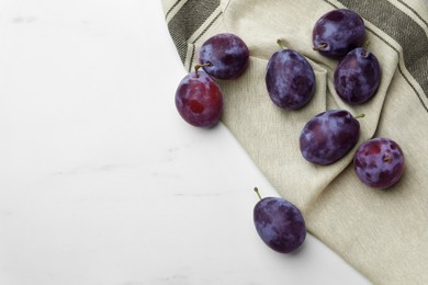 Photo of Tasty ripe plums on white marble table, flat lay. Space for text
