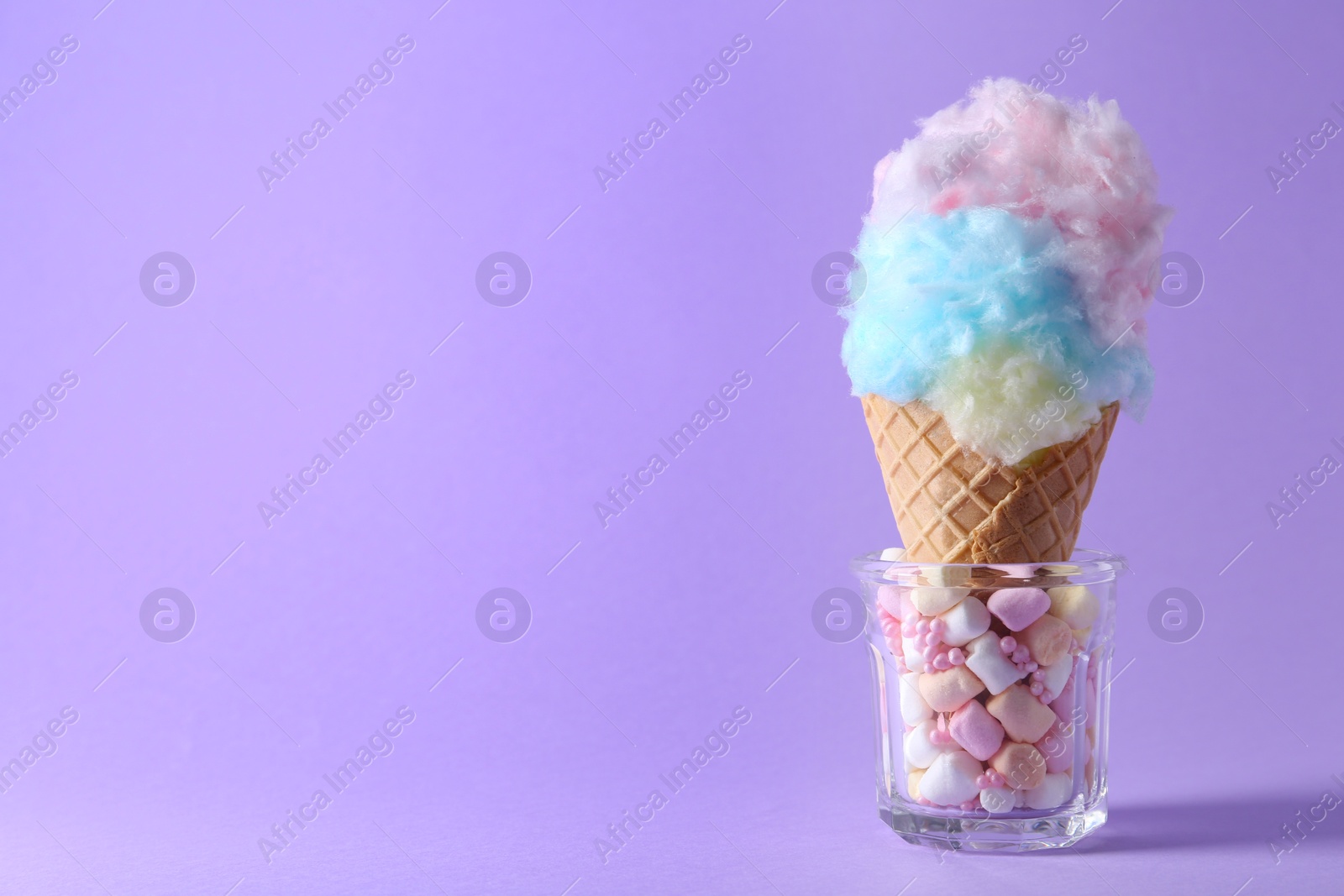 Photo of Sweet cotton candy in waffle cone on purple background, closeup. Space for text