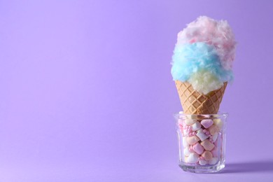 Photo of Sweet cotton candy in waffle cone on purple background, closeup. Space for text