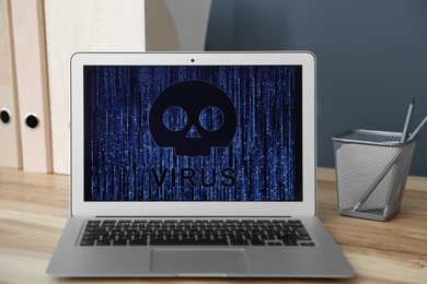 Photo of Laptop with virus illustration on wooden table in office
