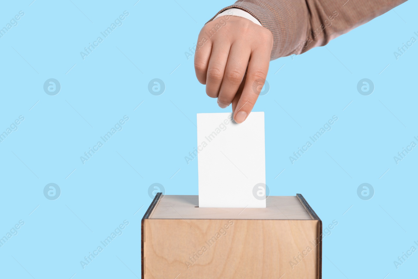 Photo of Woman putting her vote into ballot box on light blue background, closeup. Space for text