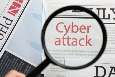 Newspaper with headline CYBER ATTACK, view through magnifying glass