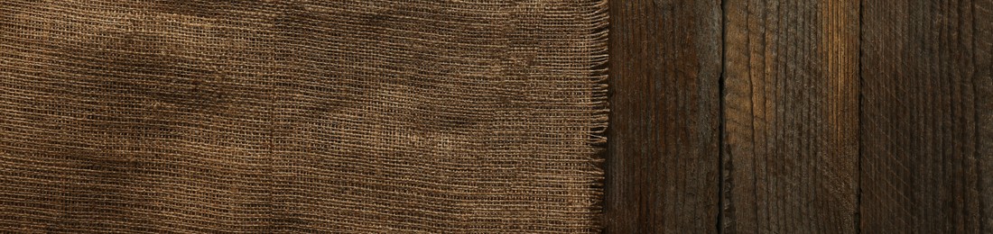 Photo of Burlap fabric on wooden table, top view. Space for text