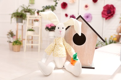 Photo of Cute toy rabbit and birdhouse on window sill indoors