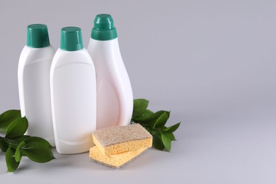 Photo of Bottles of cleaning product, sponges and green leaves on light background. Space for text