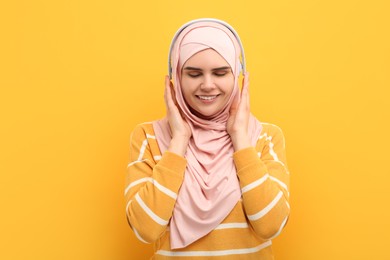 Photo of Portrait of Muslim woman in hijab and headphones on orange background