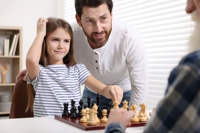 Photo of Family playing chess together at table in room