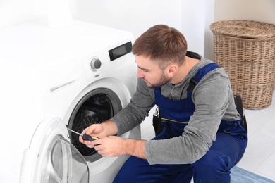 Photo of Young plumber fixing washing machine in bathroom