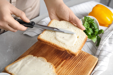 Woman spreading sauce on sandwich at light grey marble table, closeup