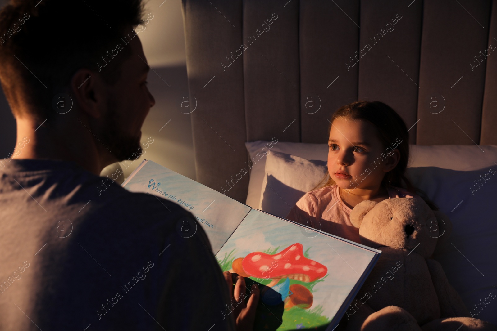 Photo of Father reading bedtime story to his daughter at home