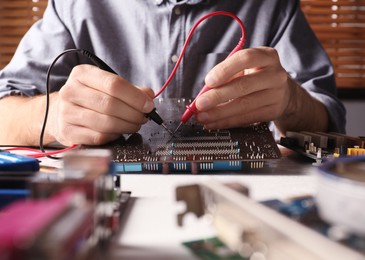Technician repairing electronic circuit board at table, closeup