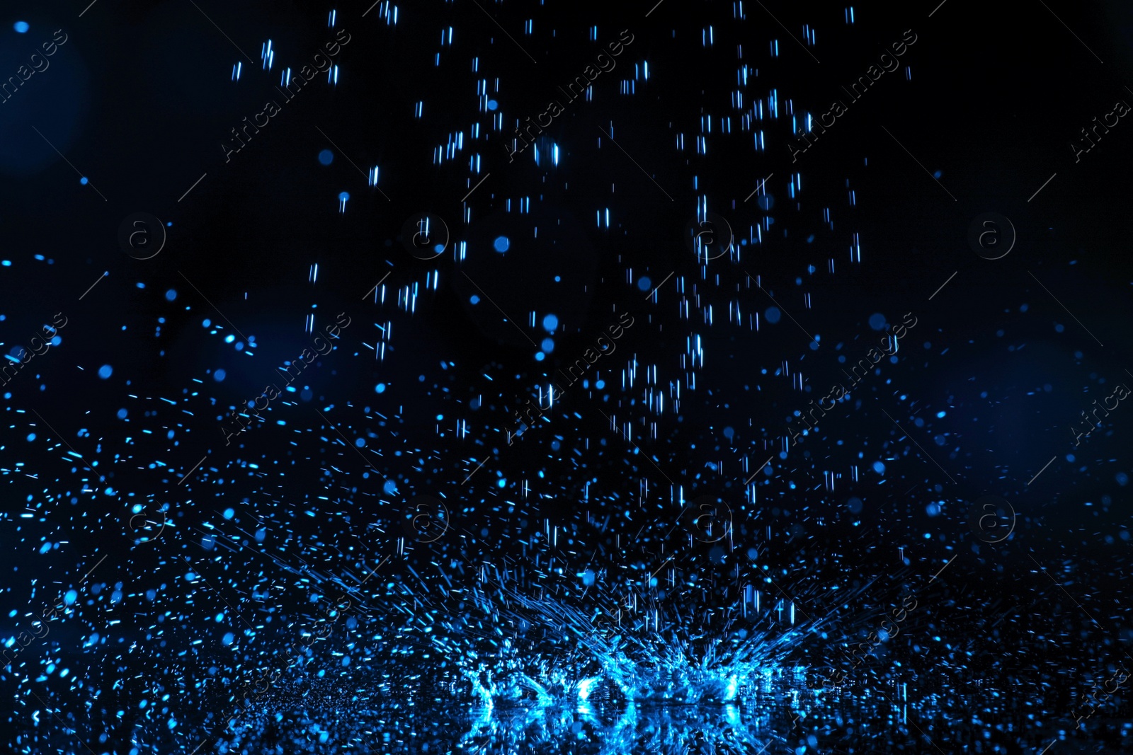 Photo of Heavy rain falling down on ground against dark background, toned in blue