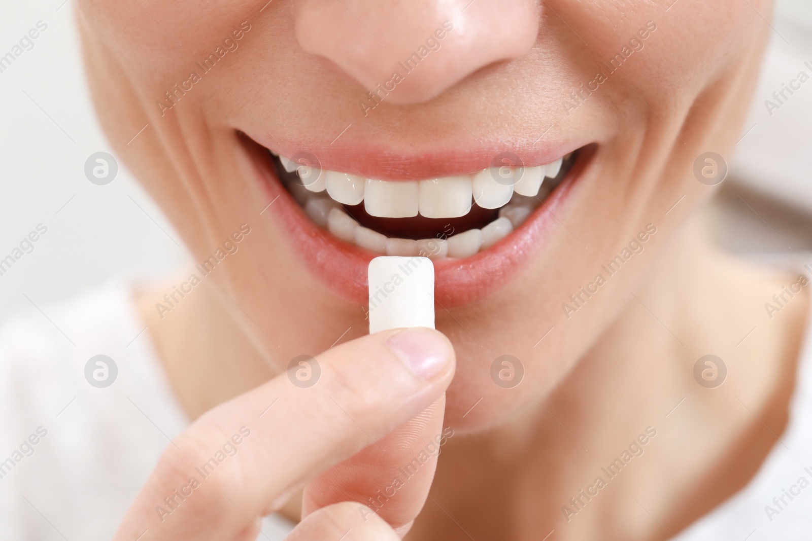 Photo of Woman putting chewing gum into mouth on blurred background, closeup