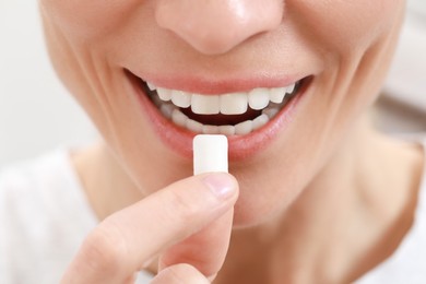 Photo of Woman putting chewing gum into mouth on blurred background, closeup