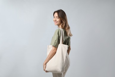 Happy young woman with blank eco friendly bag on light background