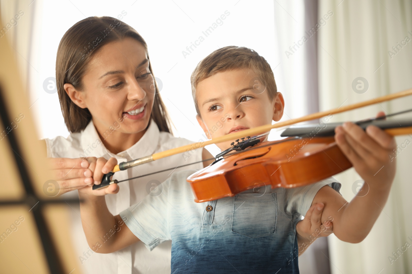 Photo of Young woman teaching little boy to play violin indoors