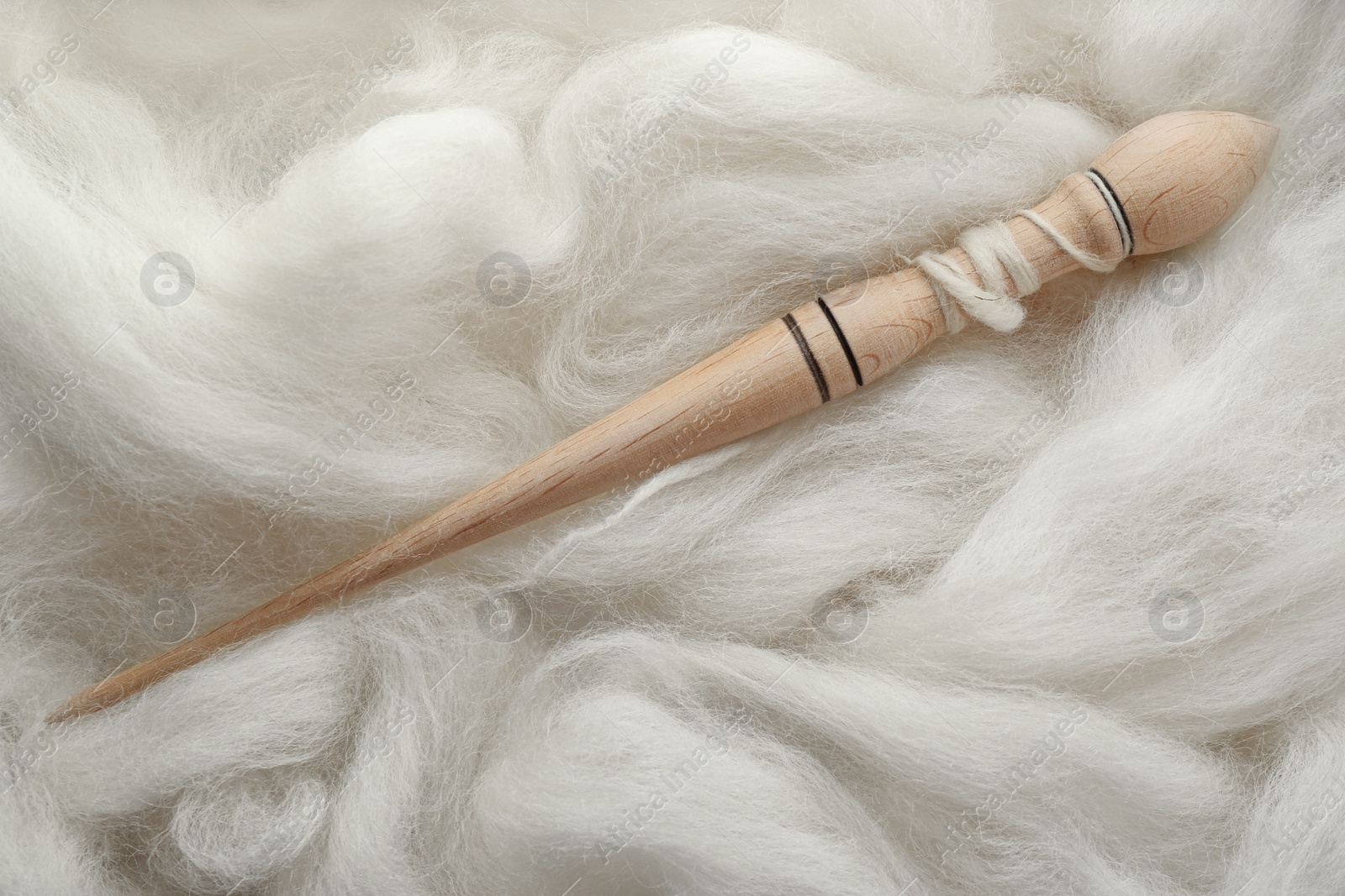 Photo of Soft white wool with spindle as background, top view