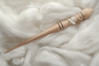 Photo of Soft white wool with spindle as background, top view