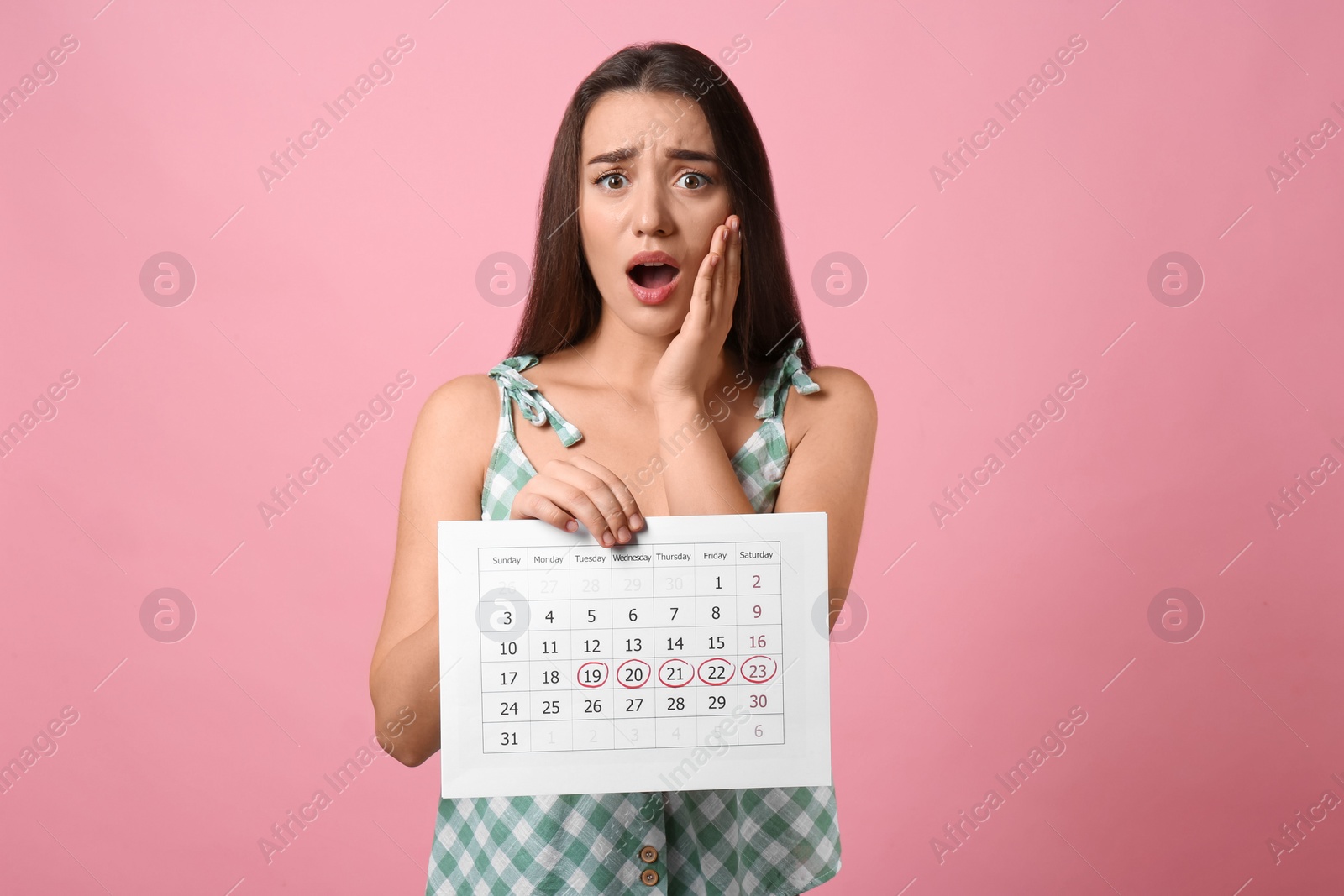 Photo of Young woman holding calendar with marked menstrual cycle days on pink background