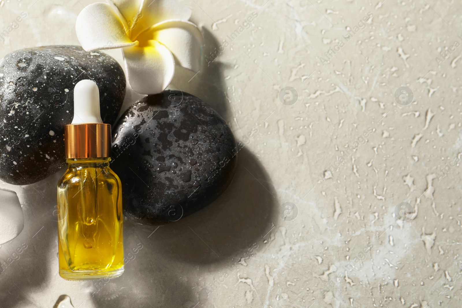 Photo of Bottle of face serum, spa stones and flower on wet grey table, flat lay. Space for text