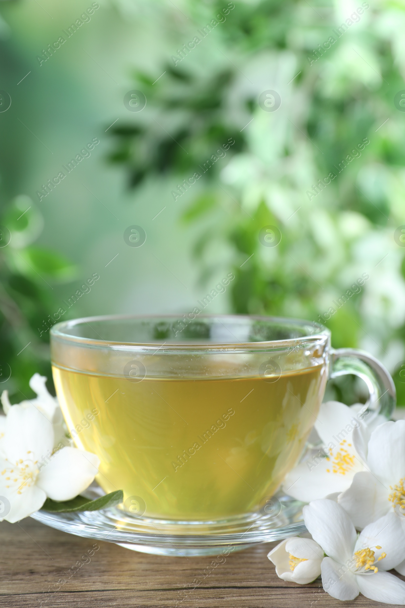 Photo of Cup of tea and fresh jasmine flowers on wooden table. Space for text