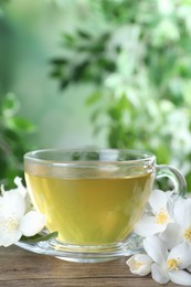 Photo of Cup of tea and fresh jasmine flowers on wooden table. Space for text