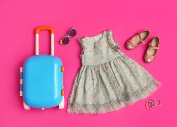 Flat lay composition with suitcase and child accessories on pink background. Summer vacation