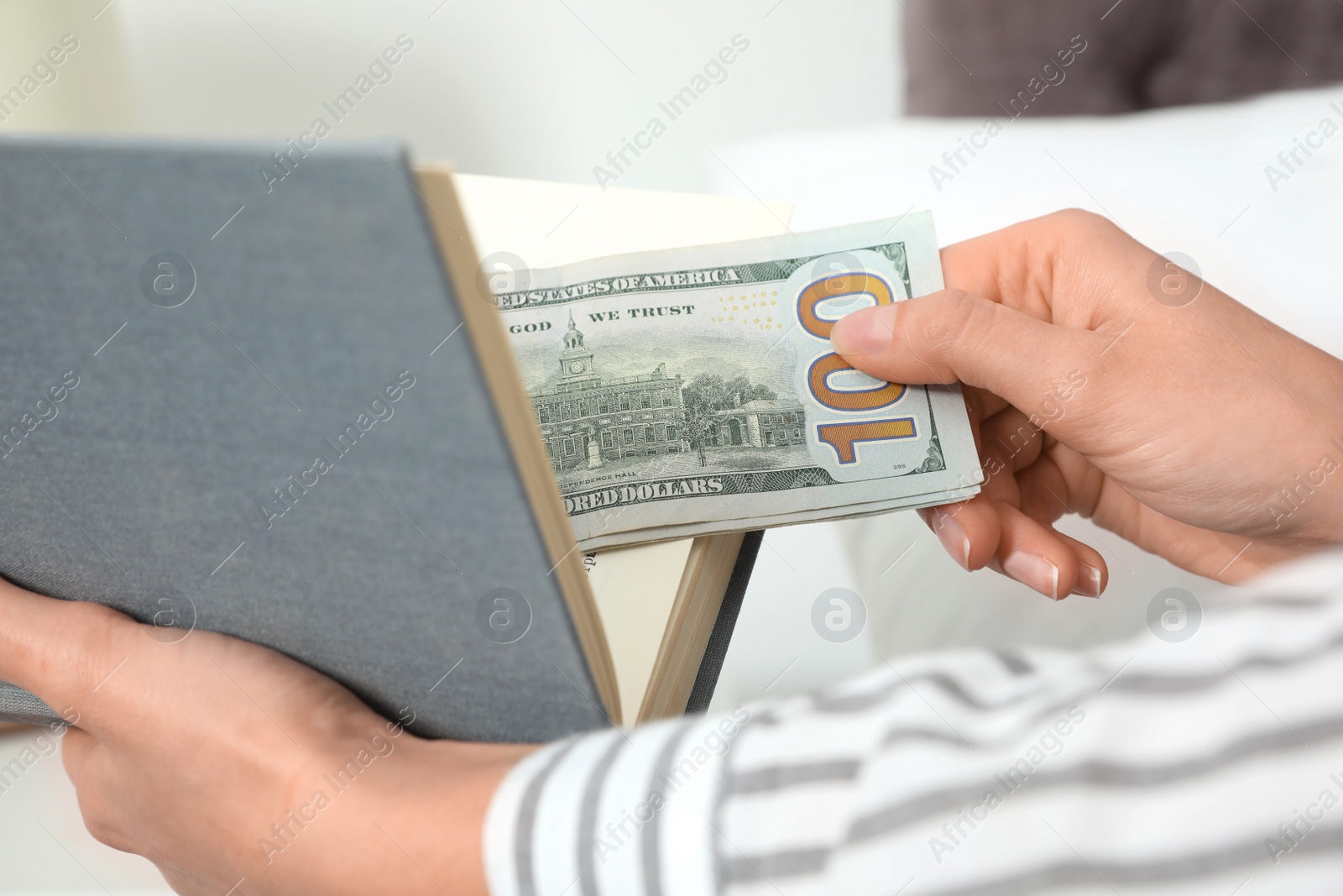 Photo of Woman hiding dollar banknotes in book indoors, closeup. Money savings