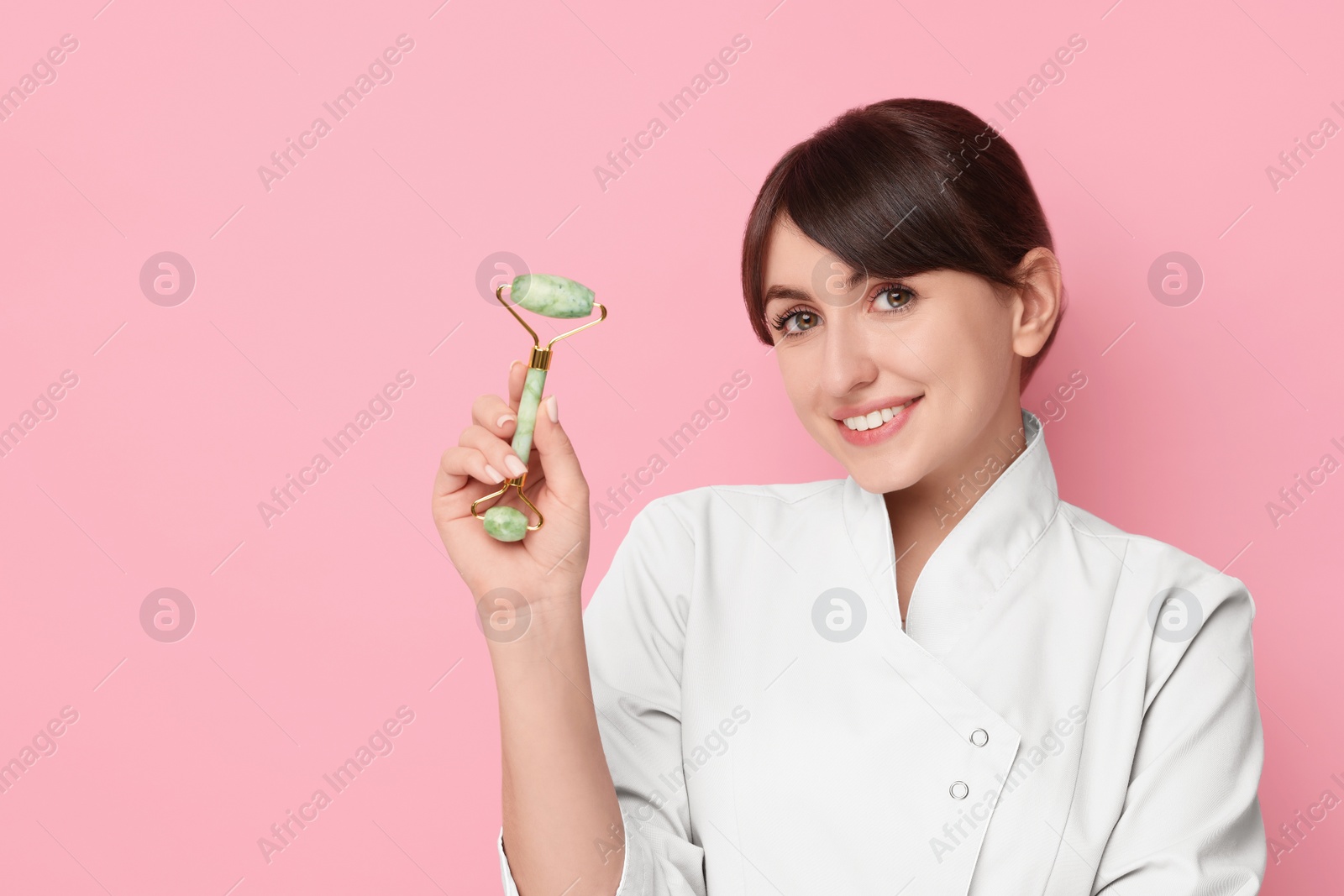 Photo of Cosmetologist with facial roller on pink background, space for text