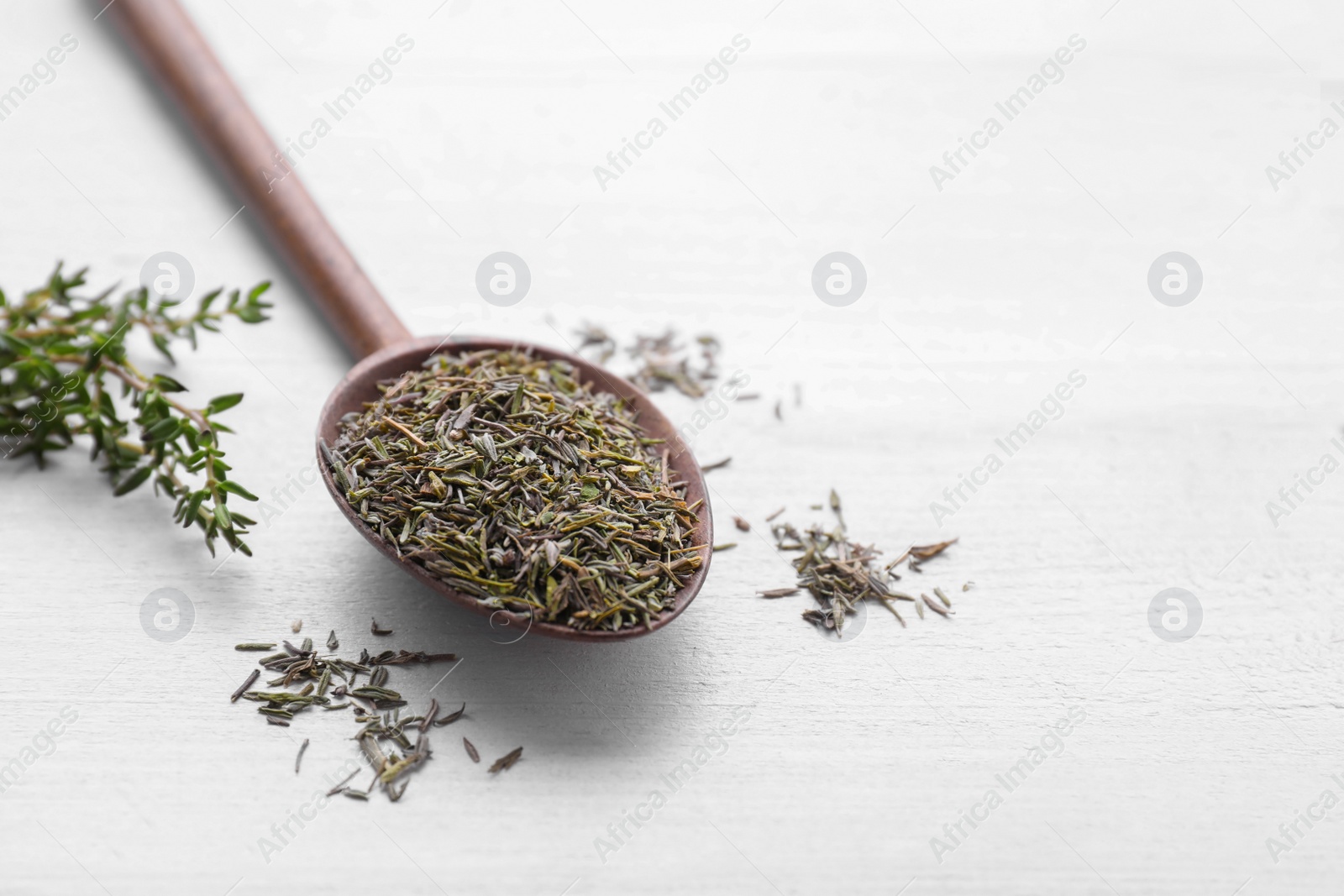 Photo of Spoon with dried thyme on white wooden table. Space for text
