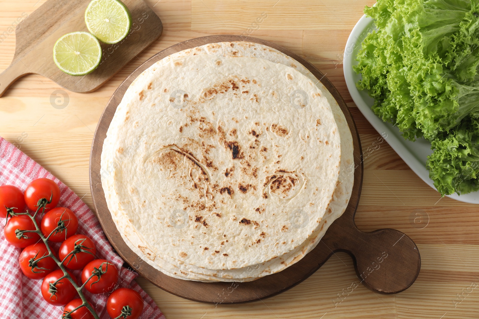 Photo of Many tasty homemade tortillas and products on wooden table, flat lay