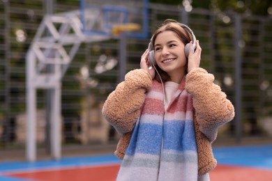 Photo of Beautiful woman in warm scarf listening to music outdoors, space for text