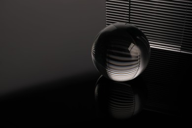 Photo of Transparent glass ball on black mirror surface. Space for text
