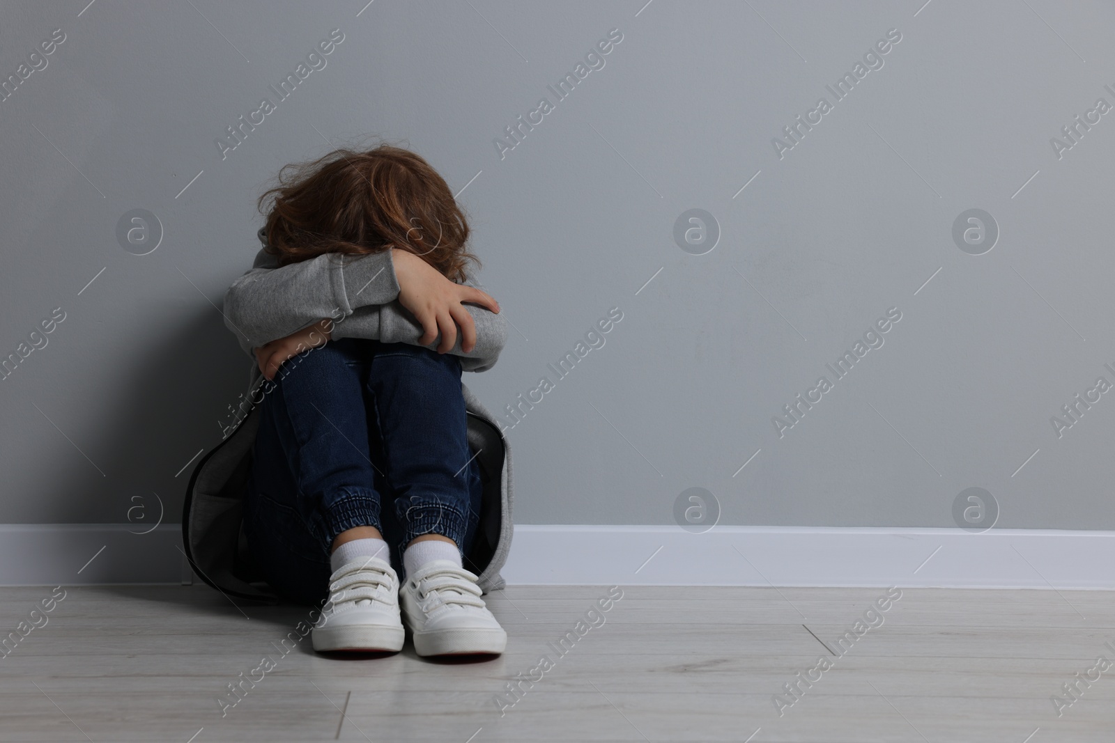 Photo of Child abuse. Upset boy sitting on floor near grey wall, space for text