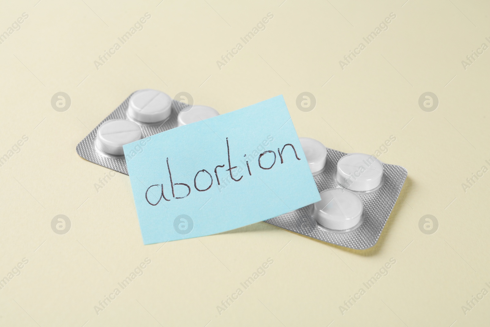 Photo of Paper note with word Abortion and pills on beige background, closeup