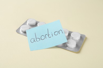 Photo of Paper note with word Abortion and pills on beige background, closeup