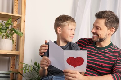 Photo of Happy man receiving greeting card from his son at home