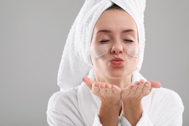Photo of Woman with cosmetic product on her face blowing kiss against grey background, space for text. Spa treatments