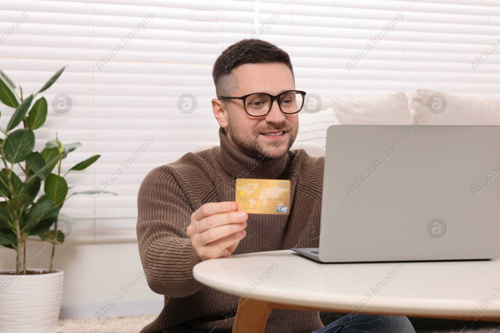 Photo of Handsome man with credit card using laptop for online shopping at home