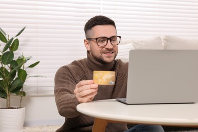 Photo of Handsome man with credit card using laptop for online shopping at home