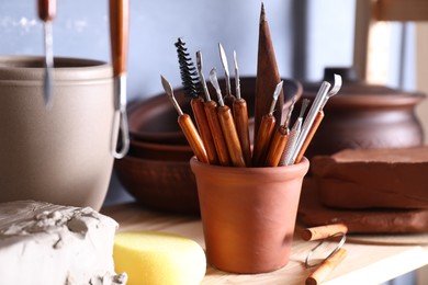 Photo of Set of different crafting tools and clay dishes on wooden rack in workshop, closeup