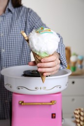 Photo of Woman holding waffle cone with cotton candy near machine, closeup. Making dessert