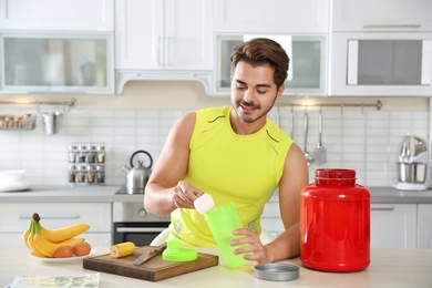 Young man preparing protein shake at table in kitchen