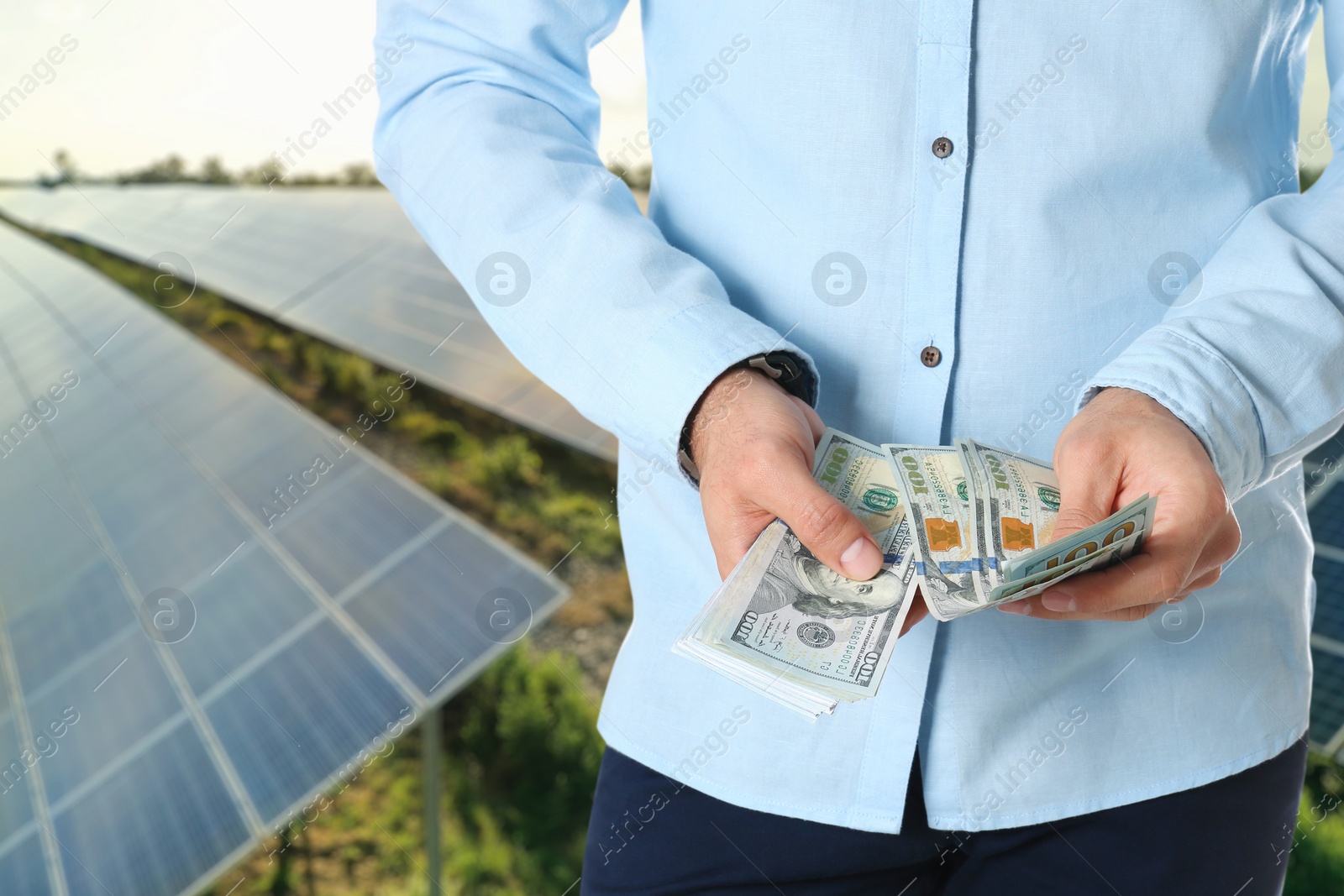 Image of Man with money and installed solar panels on background, closeup. Economic benefits of renewable energy