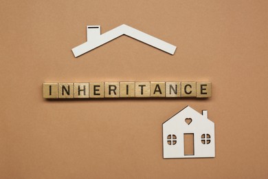 Photo of Word Inheritance made with wooden cubes and house model on brown background, flat lay