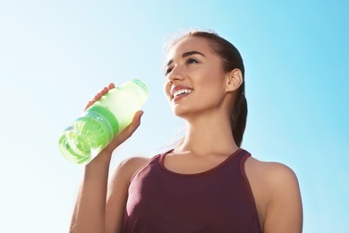 Photo of Young sporty woman drinking water from bottle against blue sky on sunny day