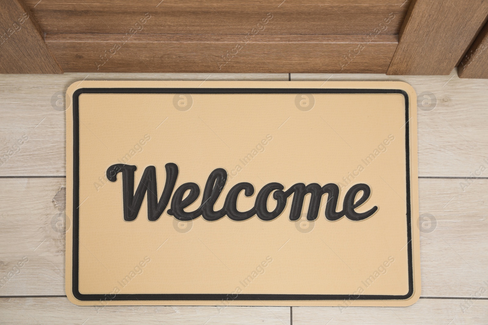 Photo of Beautiful beige doormat with word Welcome on floor near entrance, top view