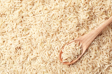 Wooden spoon with cereal on raw brown rice, top view. Space for text