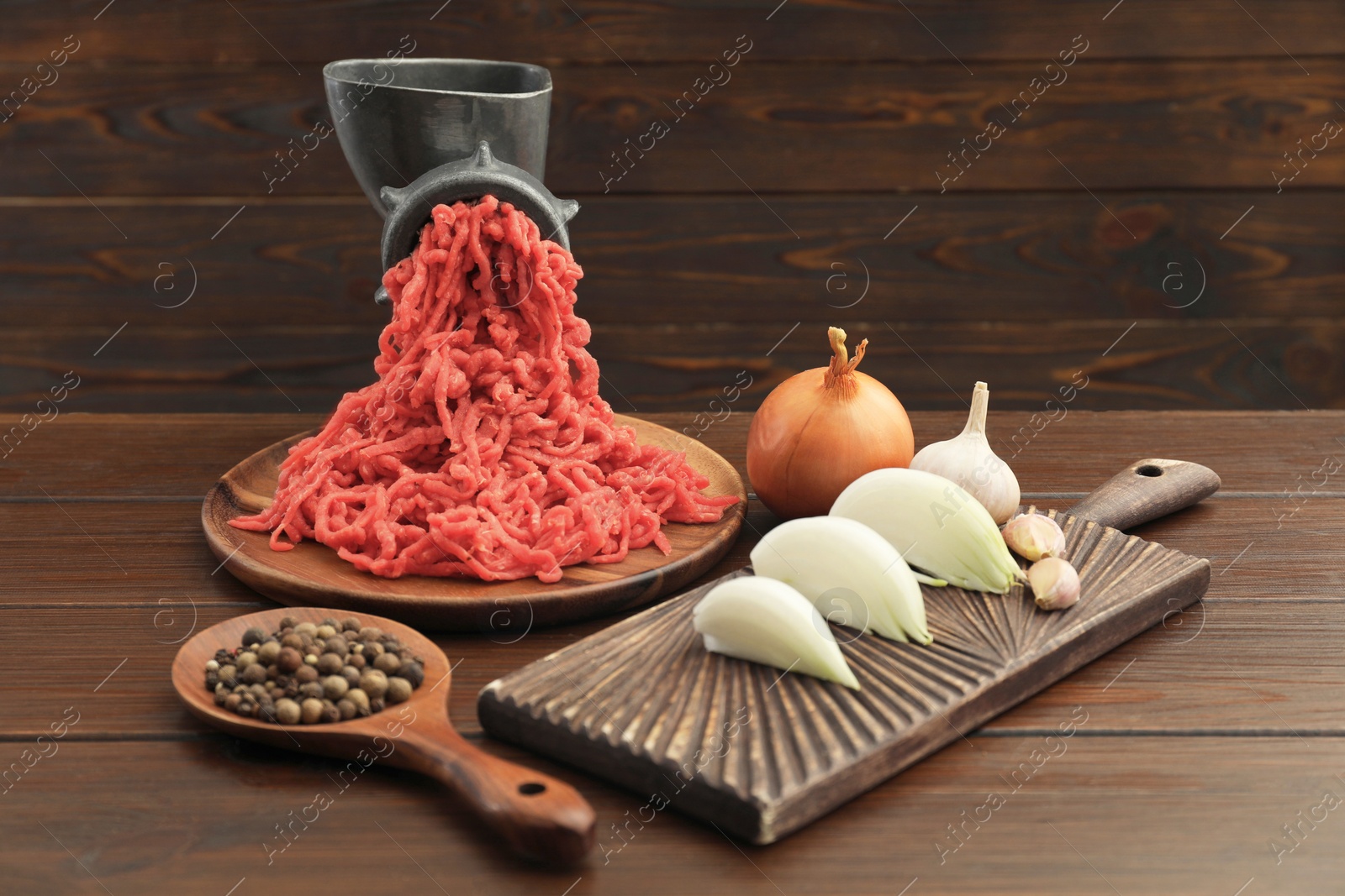 Photo of Meat grinder with beef mince, garlic, onion and peppercorns on wooden table