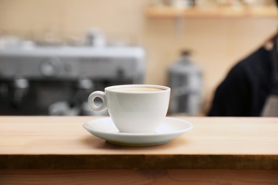 Photo of Cup of fresh aromatic coffee on table against blurred background